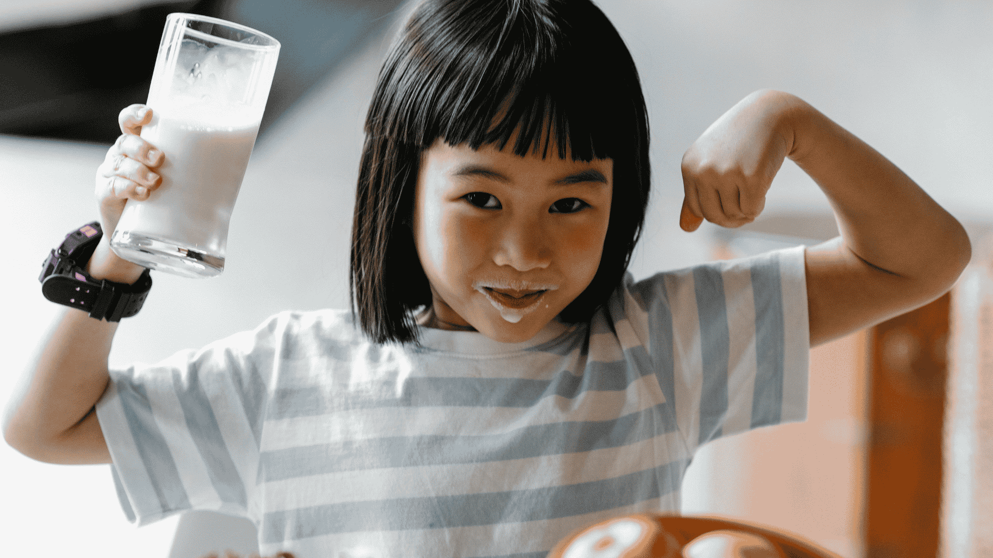 小孩手拿牛奶並比出手臂肌肉姿勢，呈現牛奶與兒童成長營養補充情境。